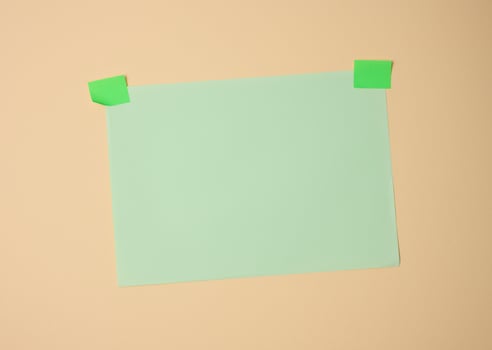 rectangular blank green sheet of paper glued with green sticky paper on light brown background photo