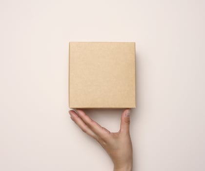 Female hand holding a square cardboard box on a beige background photo