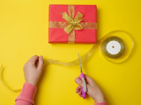 female hands are cutting a silk ribbon with scissors, next to gift boxes. Yellow background, top view photo