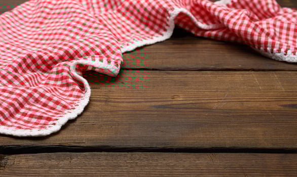 folded red and white cotton kitchen napkin on a wooden brown background, top view photo