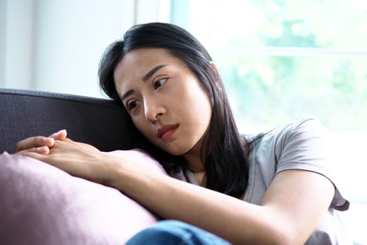 A beautiful Asian middle-aged woman has a sad and depressed expression on the couch in the house. photo