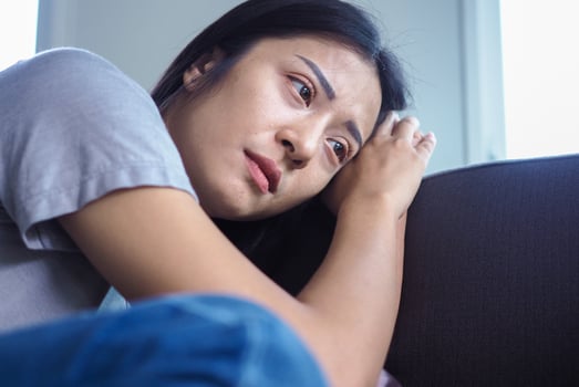 Asian woman sitting inside the house looking out at the window. Woman confused, disappointed, sad and upset photo