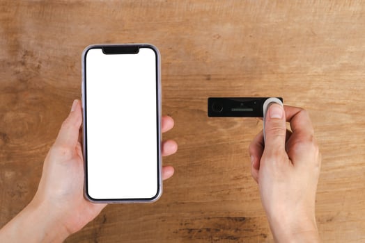 Hand holding mobile phone and hardware wallet on wooden table photo