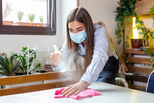 Waitress wearing protective face mask while disinfecting tables at restaurant or caffee for next customer. Corona virus and small business is open for work concept. photo