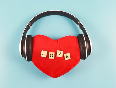 flat lay of red heart pillow with wooden letter L O V E  coverd with headphones on blue  background. Love songs , podcast or valentines concept. photo