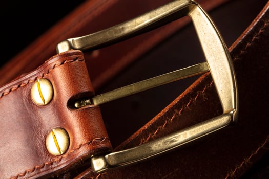 Part of a leather brown belt with a metal buckle on a black background. photo