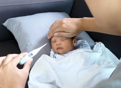 Sick baby lying on the sofa mother touch body and used the thermometer to check the temperature. photo