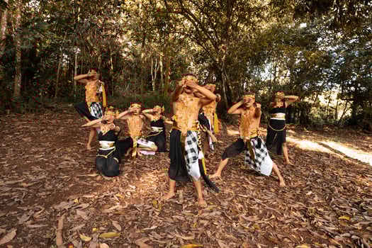 Balinese dancers with golden costumes and stripped pants dance together with the dead brown leaves in the yard photo