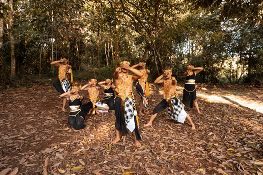 Balinese dancers with golden costumes and stripped pants dance together with the dead brown leaves in the yard photo