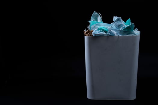 Face mask in trash sanitary napkins, plastic. Medical waste unhygienic management concept. Disposal earloop face mask waste in garbage trash. Disgusting trash bin with medical waste backgound on black photo