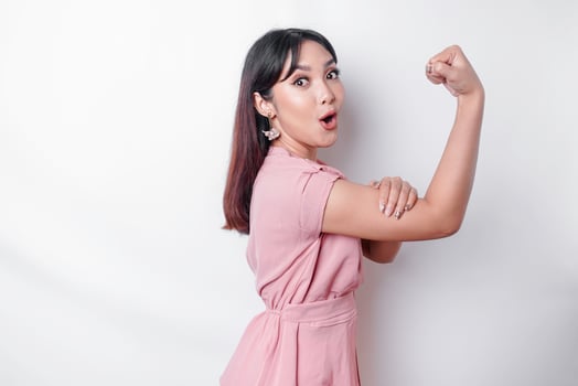 Excited Asian woman wearing a pink blouse showing strong gesture by lifting her arms and muscles smiling proudly photo