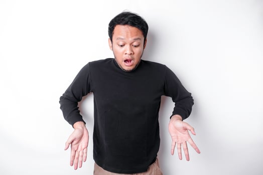 Shocked Asian man wearing black shirt, pointing at the copy space below him, isolated by white background photo