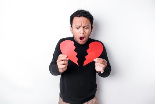 Beautiful young Asian man expressed his sadness while holding broken heart isolated on white background photo