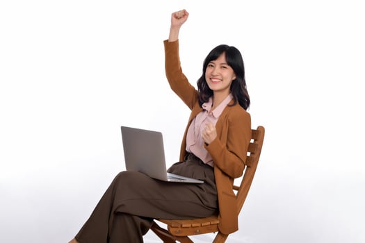 Happy young business asian woman celebrating on her success. While her using laptop sitting on wooden chair isolate on white background photo