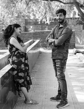 Indian couple posing for maternity baby shoot. The couple is posing in a lawn with green grass and the woman is falunting her baby bump in Lodhi Garden in New Delhi, India - Black and White photo