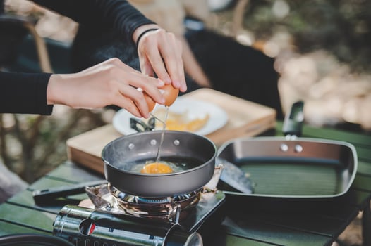 Young woman cooking with egg while camping with girl friend photo