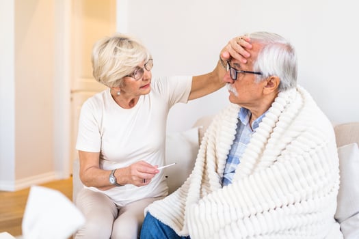 Woman checking fever temperature of senior man. Old husband resting at home feeling sick while his wife checking fever by touching forehead photo