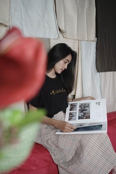 Asian woman from Indonesia sits and reads a book against a colorful cloth background. photo