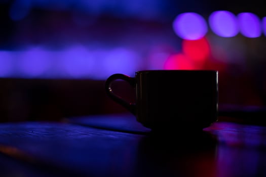 Cup on table in bar. Coffee mug in restaurant. Drink cup in purple light. Interior details. photo
