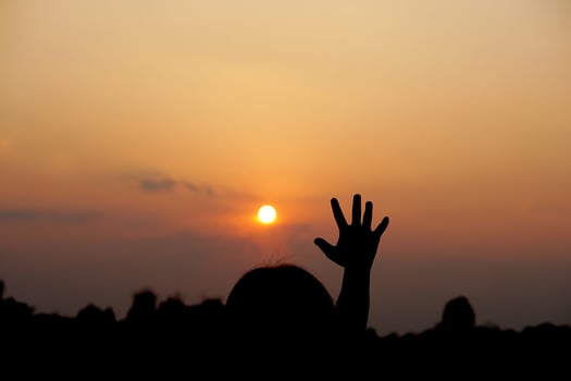 silhouette of human hand raised to make a wish, sunset background photo