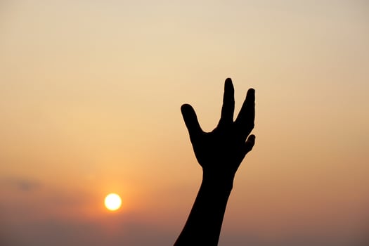 silhouette of human hand raised to make a wish, sunset background photo