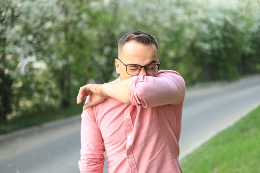 A man sneezes in the park while she walks in the park. Allergy, flu, virus concept. photo
