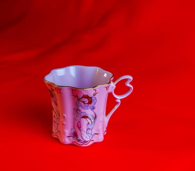 Porcelain pink cup of an unusual shape is made in the Czech Republic. A cup with a romantic pattern on a red background. photo