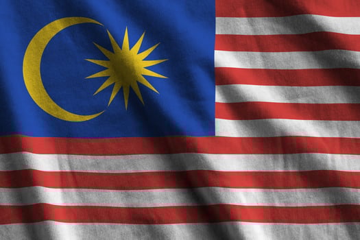Malaysia flag with big folds waving close up under the studio light indoors. The official symbols and colors in banner photo