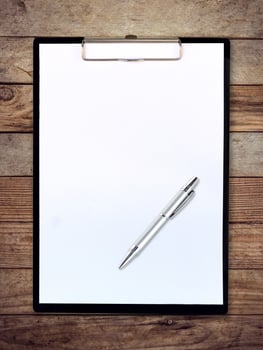 white paper clipboard on wood background with pen photo