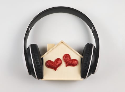 flat lay of wooden model house with two red glitter hearts covered with headphones isolated on white  background. music or podcast, home of love, valentines. photo