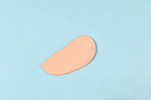 Makeup liquid foundation, beige concealer smear. Light brown cosmetic makeup base cream swatch smudge isolated on blue background. BB CC cream texture photo