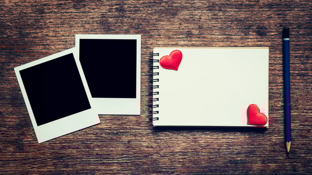Blank photo frame, notebook, pencil and red heart on wood table background.
