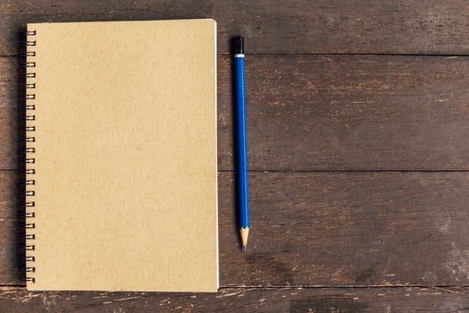 brown book and pencil on wood table background with space photo