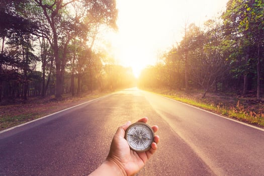 Hand holding compass on empty asphalt road and sunset. photo