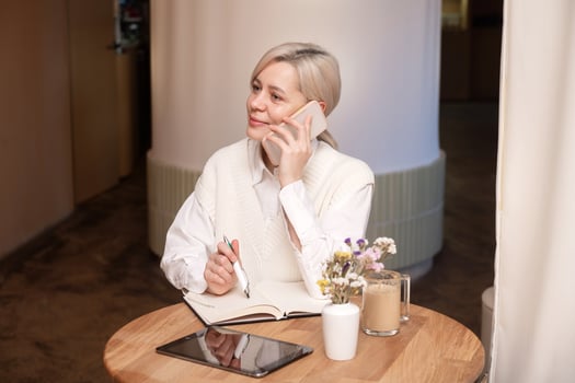 A cute girl is sitting in a cafe and talking on the phone and making notes in a diary photo