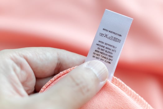 Hand hold and reading at white laundry care washing instructions clothes label on pink shirt photo