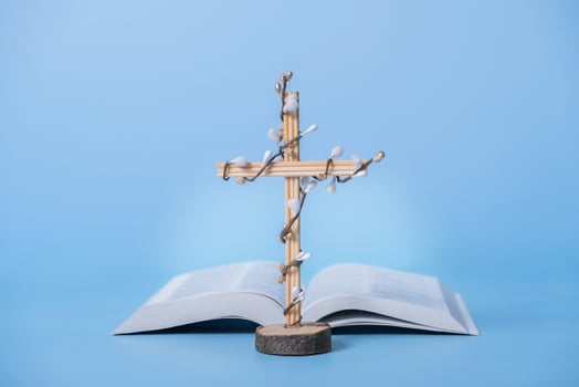 Cross decorated flowers with Holy Bible on blue background. Easter holiday minimalistic concept photo