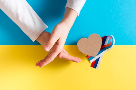 The concept is no war in Ukraine. Children's hands show a cross, a cardboard heart and a ribbon of the Russian flag against the background of the Ukrainian flag. Top view. photo