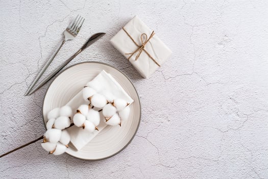 Plate, cutlery, gift and cotton branch on a textured gray background. Eco serving. Top view. photo