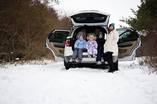 Mother with three children sit on car suv with open trunk stand in winter forest. photo