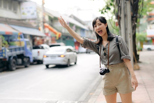 Smiling young Asian woman traveler hitchhiking on a road in the city. Life is a journey concept. photo