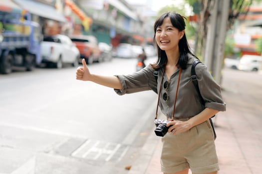Smiling young Asian woman traveler hitchhiking on a road in the city. Life is a journey concept. photo