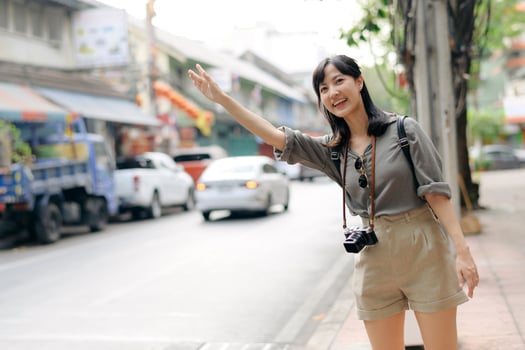Smiling young Asian woman traveler hitchhiking on a road in the city. Life is a journey concept. photo
