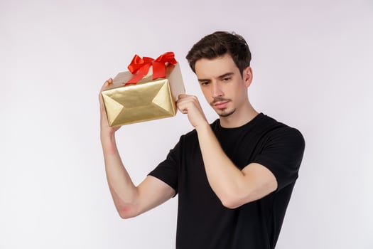 Portrait of confused young caucasian man showing present box and looking at camera isolated over white background. Birthday party concept. photo