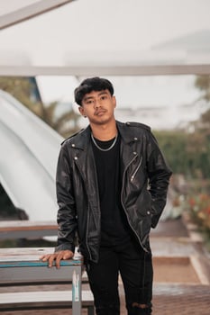 a grown man in a black leather suit and chain necklace posing very dashingly in the broad photo