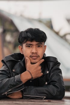 an Asian man with a naughty face wearing a chain necklace and a black leather jacket in a cafe photo
