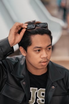 an Asian man is sitting on a wooden chair while wearing a black leather shirt and jacket while stylish with sunglasses photo