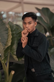 an asian boy in a black denim jacket posing like a naughty boy with a chain around his neck in a park photo