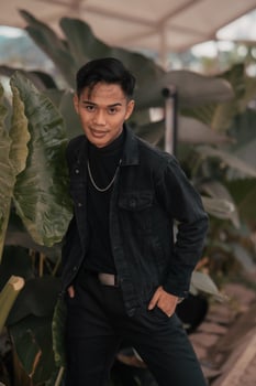 an asian boy in a black denim jacket posing like a naughty boy with a chain around his neck in a park photo