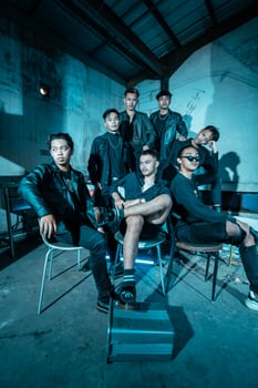 a group of Asian teenagers in black clothes posing very coolly while sitting in a warehouse chair which is lit blue photo